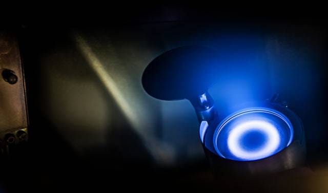 dc-sputtering-angstrom-engineering alt = A close-up of a DC sputtering process, showing a glowing blue circular plasma inside a metallic chamber. The intense blue light highlights the advanced physical vapor deposition technique used for coating materials.